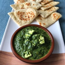 Round naan flatbread served beside saag paneer