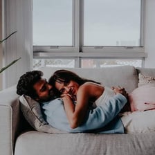 A couple curled up together affectionately on a sofa.