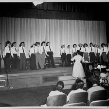 A student glee club singing together on a stage.
