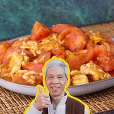 A fresh red tomato beside a dish of Chinese scrambled eggs with tomato.