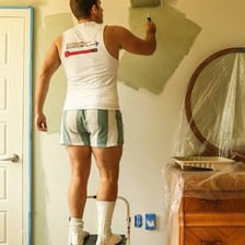 A person using a roller to apply fresh paint to an interior wall