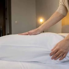 A person fluffing a pillow to make it fuller