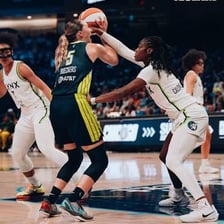 Two women’s basketball teams competing with five players from each team on the court.