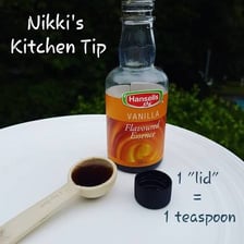 A teaspoon measuring vanilla extract over a mixing bowl