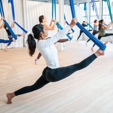 A person performing an aerial-yoga pose in a fabric hammock