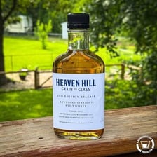 A glass of rye whiskey beside stalks of rye grain