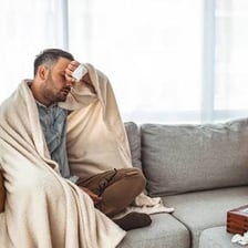 A person rests under a blanket while feeling unwell.