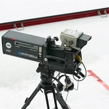 A television studio camera pointed toward a broadcast set.