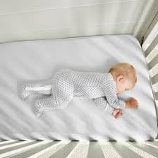 Baby sleeping in a crib covered by a fitted crib sheet