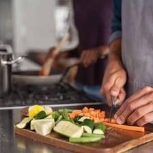 A kitchen worker chops vegetables at a restaurant prep station.
