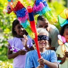 A colorful piñata hangs at a party as someone swings a stick toward it.