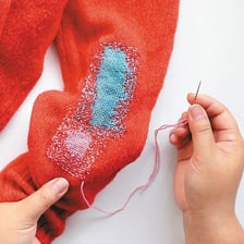 A person repairing torn fabric with a needle and thread