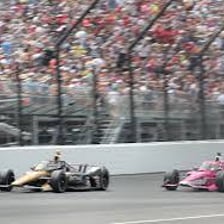 Open-wheel race cars speeding around an oval track.