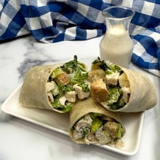 A handheld wrap filled with Caesar salad ingredients, including romaine and croutons.