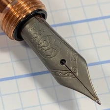 A close-up view of the pointed metal nib of a fountain pen.