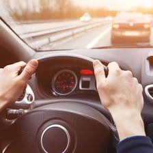 A driver steering a car along a road.