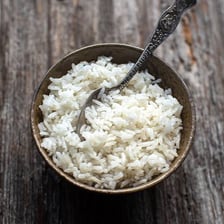 A bowl of cooked rice with rice plants in the background.