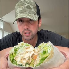 A person eating a Caesar salad wrap.