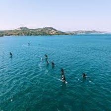 A coastal sea with swimmers and a sailboat.