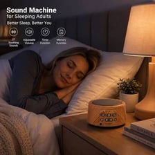 A white-noise machine beside a bed in a quiet bedroom.