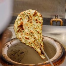 Naan bread being baked inside a tandoor oven