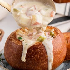 A ladle serving chowder from a pot into a bowl.
