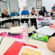 Actors seated around a table reading from scripts during a rehearsal