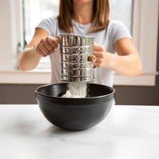 A handheld kitchen sieve being used to sift flour.