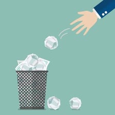 A person tossing discarded paper into a waste bin