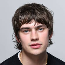 A person with a thick, shaggy hairstyle resembling a mop
