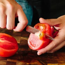 A person trimming a vegetable with a knife.