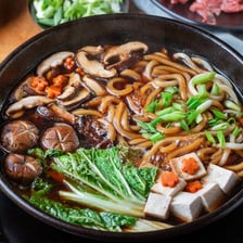 A bowl of sukiyaki containing thick udon noodles.