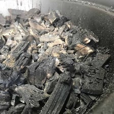 Gray ash remaining among the coals of a charcoal grill.