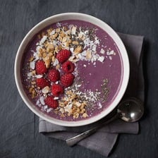 Dark purple açaí berries beside an açaí smoothie bowl.