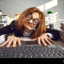 A person with glasses surrounded by computers and books