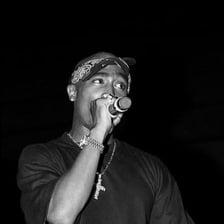 A portrait of rapper Tupac Shakur performing with a microphone.