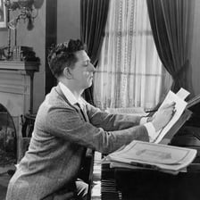 A person writing music while seated at a piano