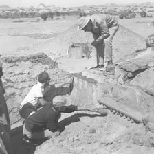Archaeologists carefully excavating a marked dig site.