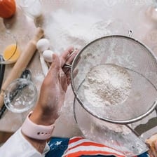 Hands shaking flour through a kitchen sieve
