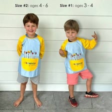 A child wearing an art smock during a glitter-glue craft activity.