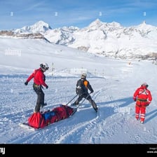 Ski patrollers in rescue gear working on a snowy slope.