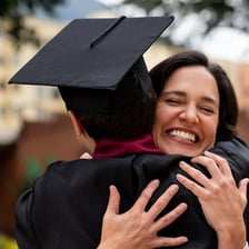 A parent celebrating beside a graduate at a graduation ceremony.