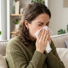 A person sneezing into a tissue