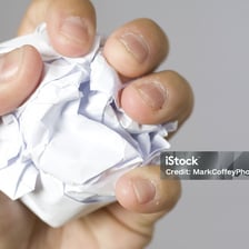 Hands compressing a sheet of paper into a crumpled wad.