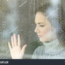 A person gazing out a window with a wistful expression