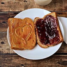 Peanut butter and jelly being spread on slices of bread.