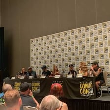 A convention panel with speakers seated on a stage before an audience.