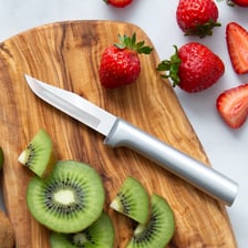 A paring knife removing the outer layer of a vegetable