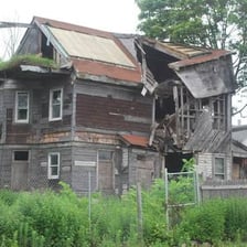 A neglected house standing out among homes in a neighborhood.