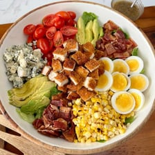 A Cobb salad topped with bacon, chopped egg, greens, and other customary ingredients.